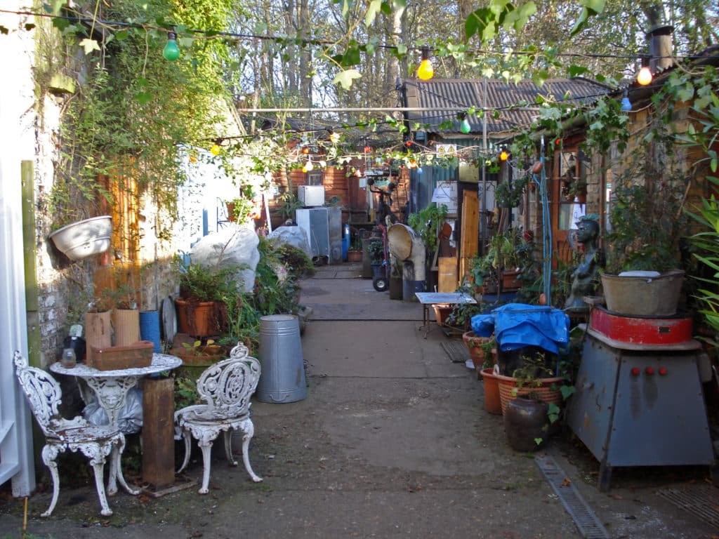 a laneway, strung over with fairy lights, and lined with trinkets and odds and ends, on Eel Pie Island