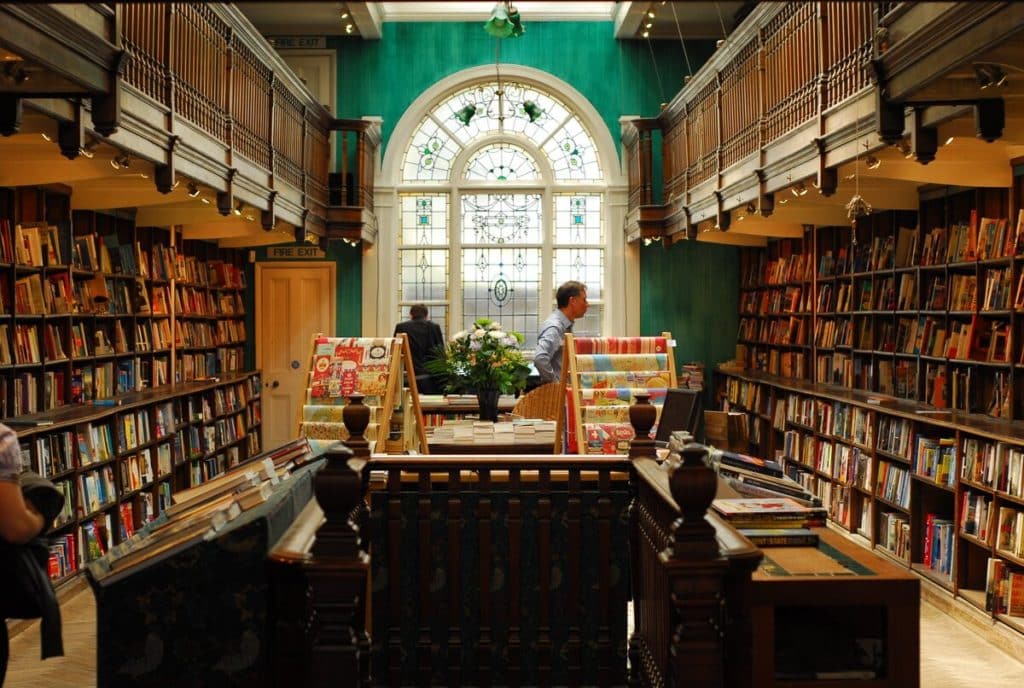 someone browsing the bookshelves at daunt books, with a large ornate window visible at the back