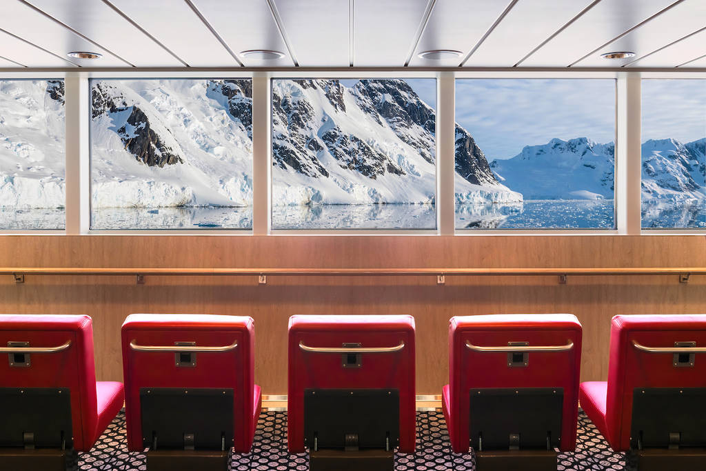 a row of red chairs in front of a big window framing a mountain scene