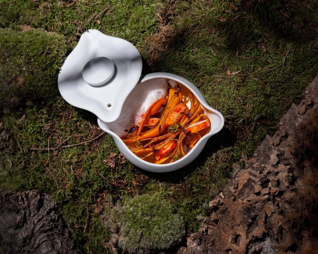 a lobster dish in a white porcelain dish presented atop a mossy setting