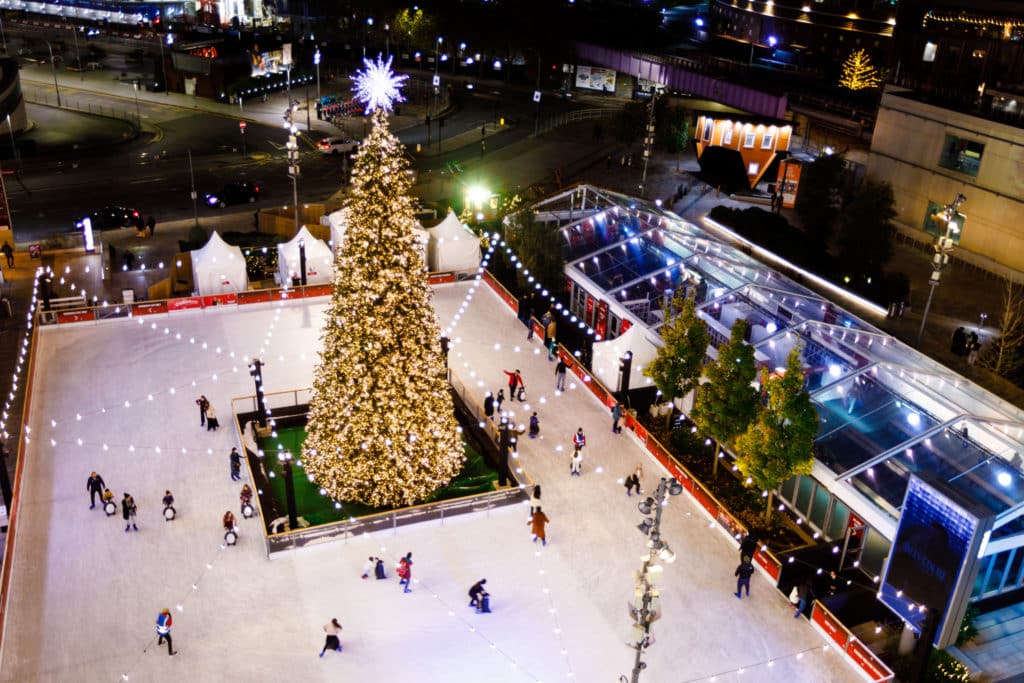 Westfield's Winter Village Ice Rink sees a massive tree in the middle of an ice skating rink, with skaters whizzing their way around it