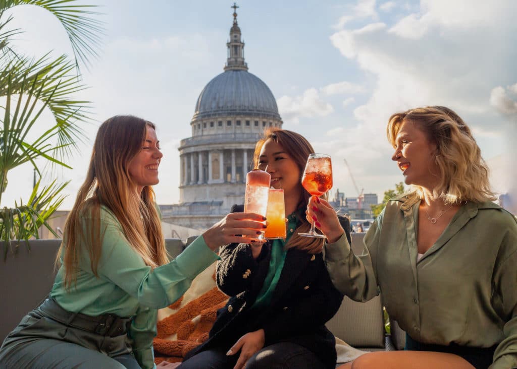 three people enjoying a drink in front of a rooftop view of St Paul's