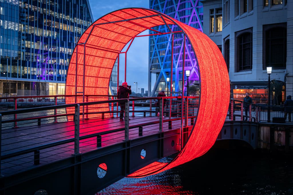 an illuminated installation surrounding a bridge walkway in canary wharf