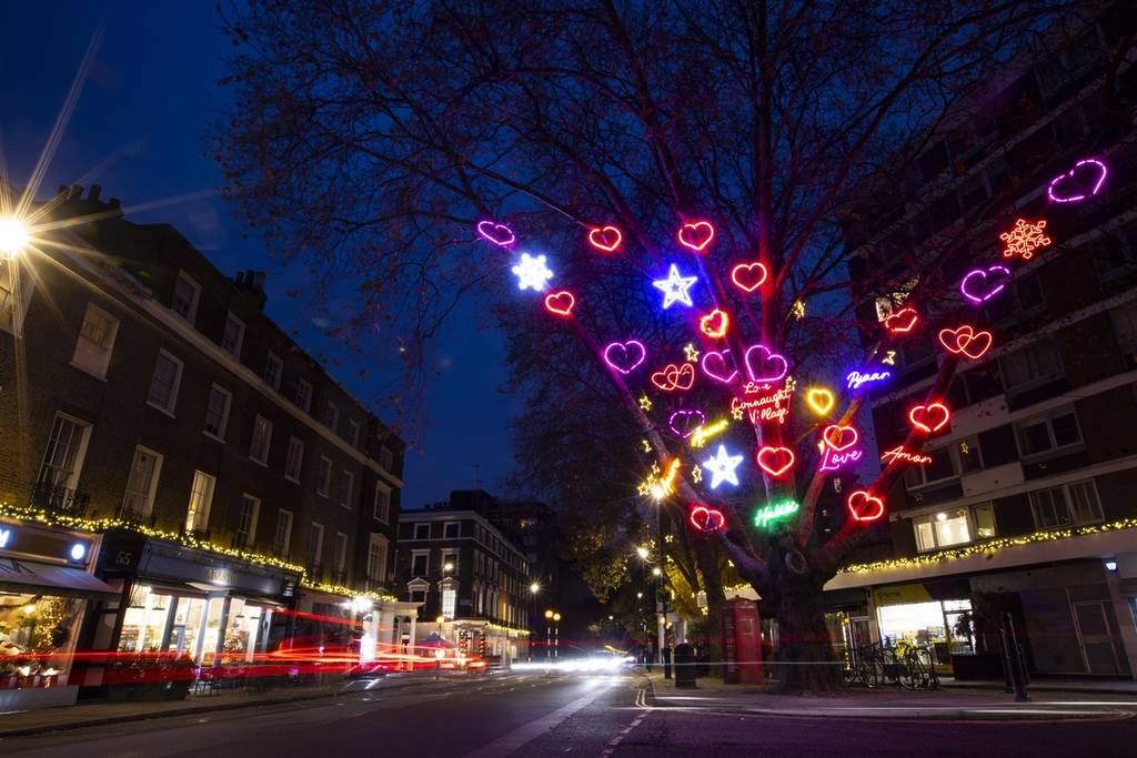the connaught village tree of love illuminated at night, displaying neon lit hearts, stars, and messages of love all over its branches