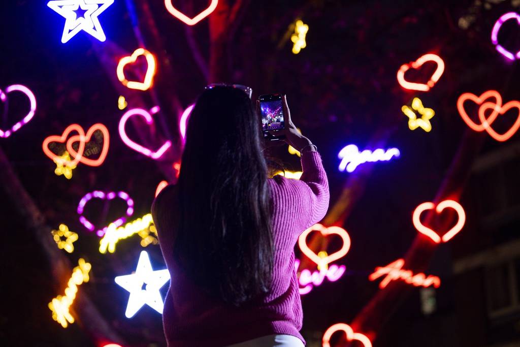 someone photographing a tree covered in neon hearts and stars and the word love written in multiple languages