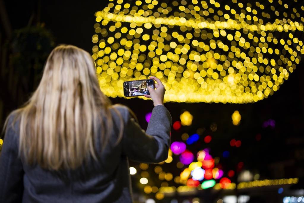 someone taking a photo of the connaught village christmas lights at night