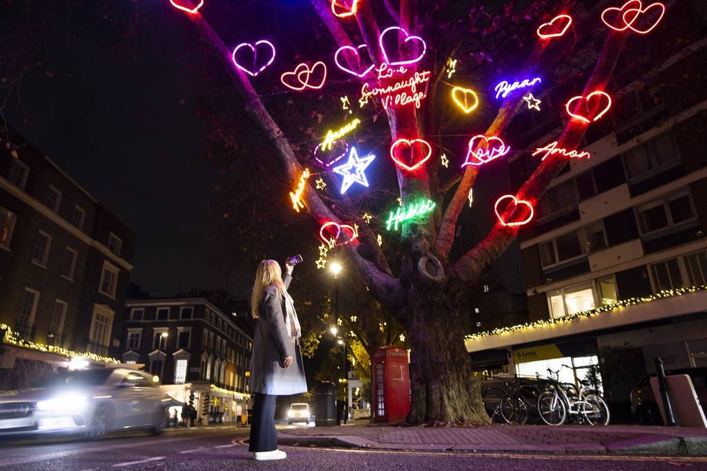 someone stood beneath the connaught village neon-lit chrsitmas tree covered in hearts and messages of love
