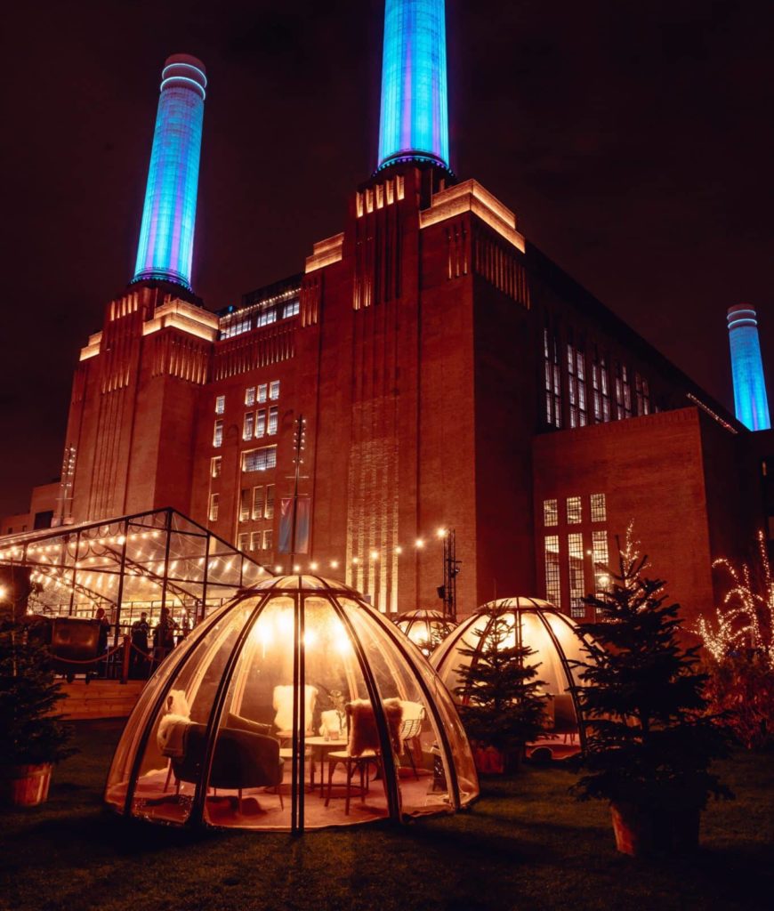 the igloos at glide at battersea at night, with battersea power station looming behind, the chimneys glowing blue