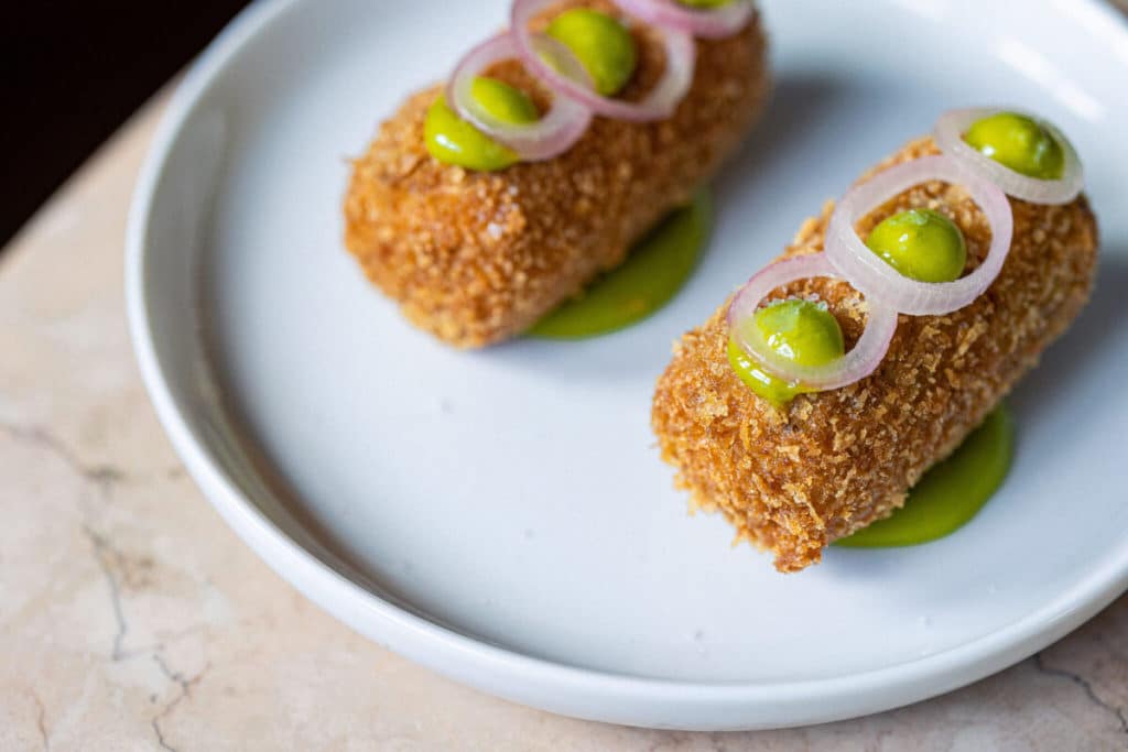 two croquettes on a white plate with green sauce and slivers of onion atop each