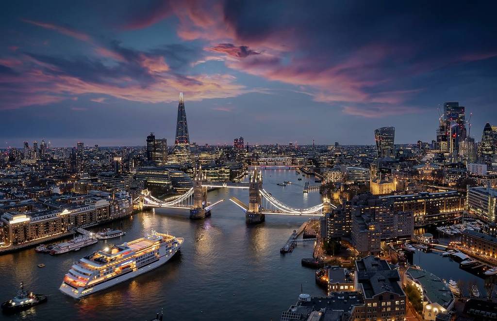 Panoramic, aerial view of the skyline of London with a motion blurred cruise ship passing under the lifted Tower Bridge during dusk