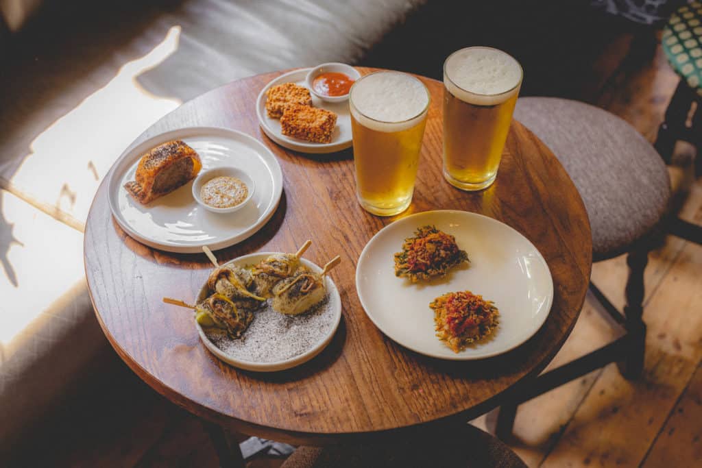 a selection of plates with bar snacks, presented next to two pints of beer