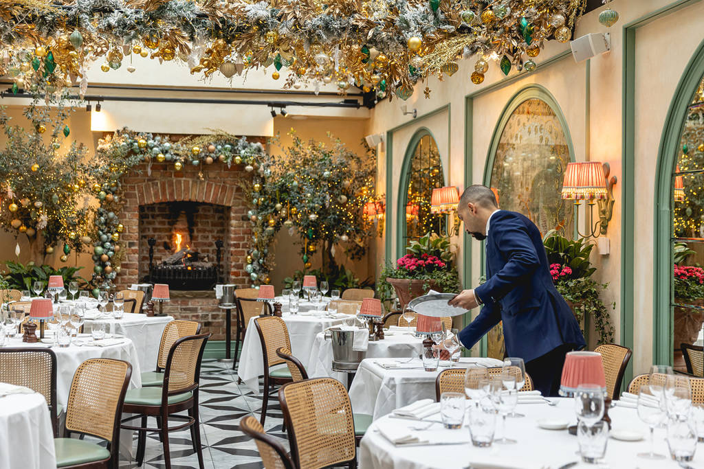someone setting the table inside daphne's gorgeously christmassy dining room, where every inch of the ceiling has been festooned with festive decor