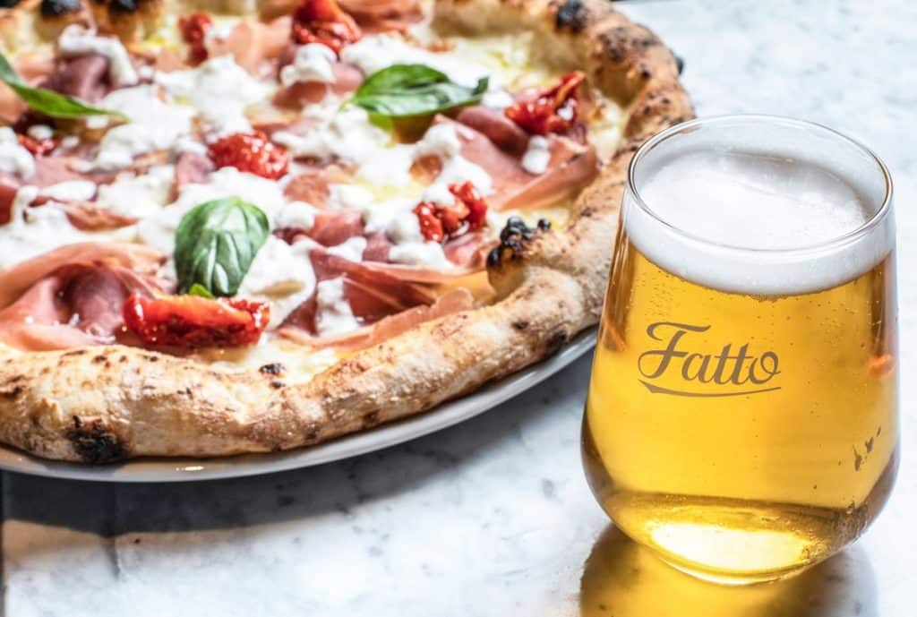 a golden hued glass of beer next to a pizza topped with ham and cheese and fresh basil from one of LOndon's newest pizza places, Fatto A Mano in King's Cross