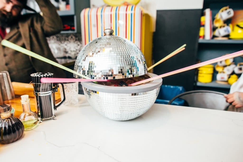 A cocktail served in a hollowed-out disco ball, with straws protruding from it.