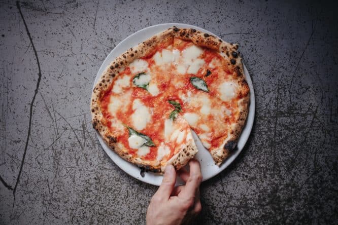 A hand grabbing a slice from a margherita pizza at Sodo in Clapton