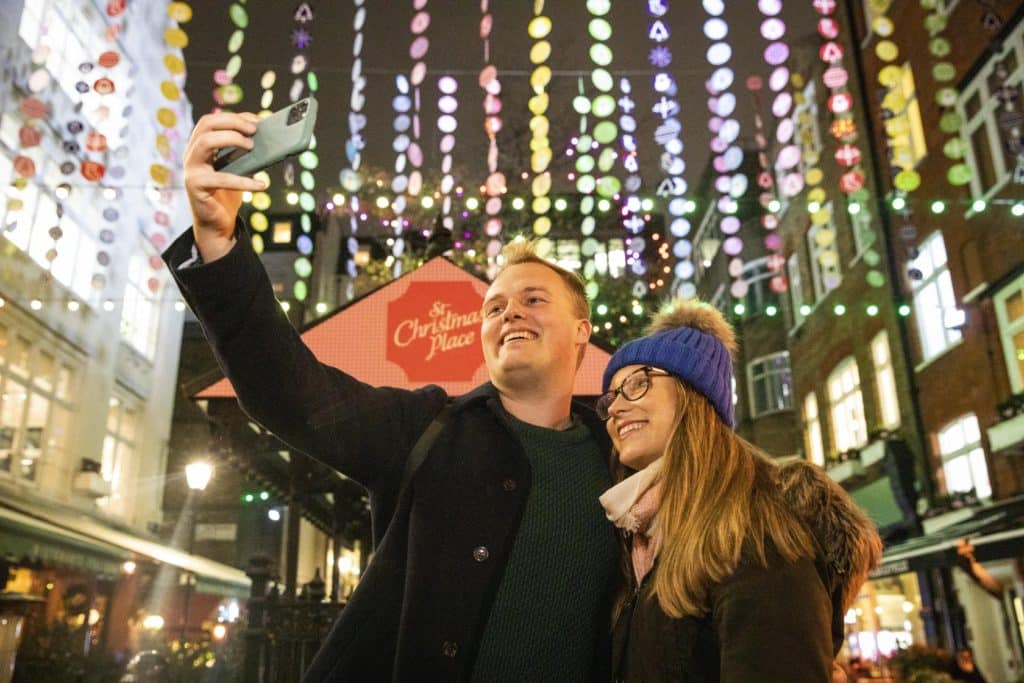 two revellers taking a photo of themselves in front of the christmas lights