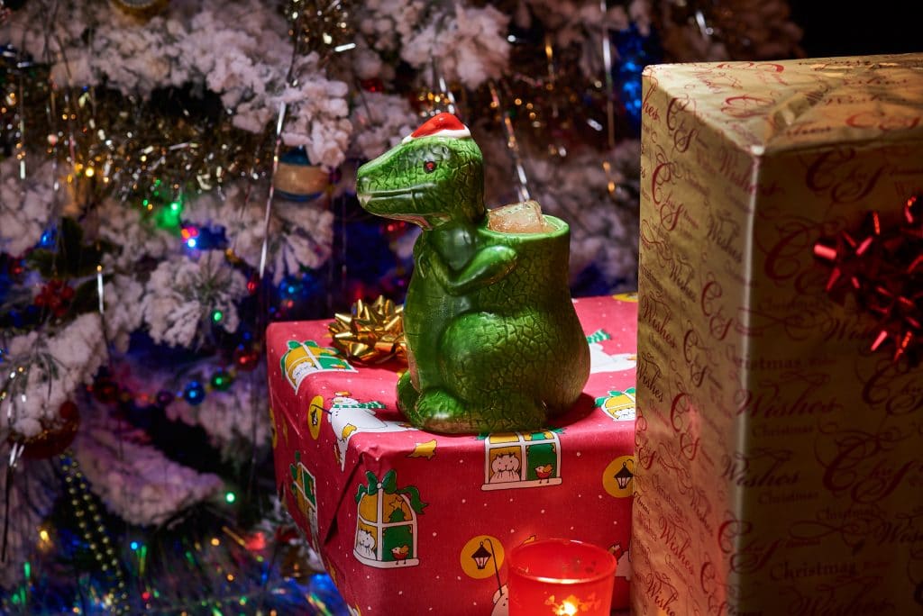a t-rex shaped mug wearing a santa hat and containing a special cocktail