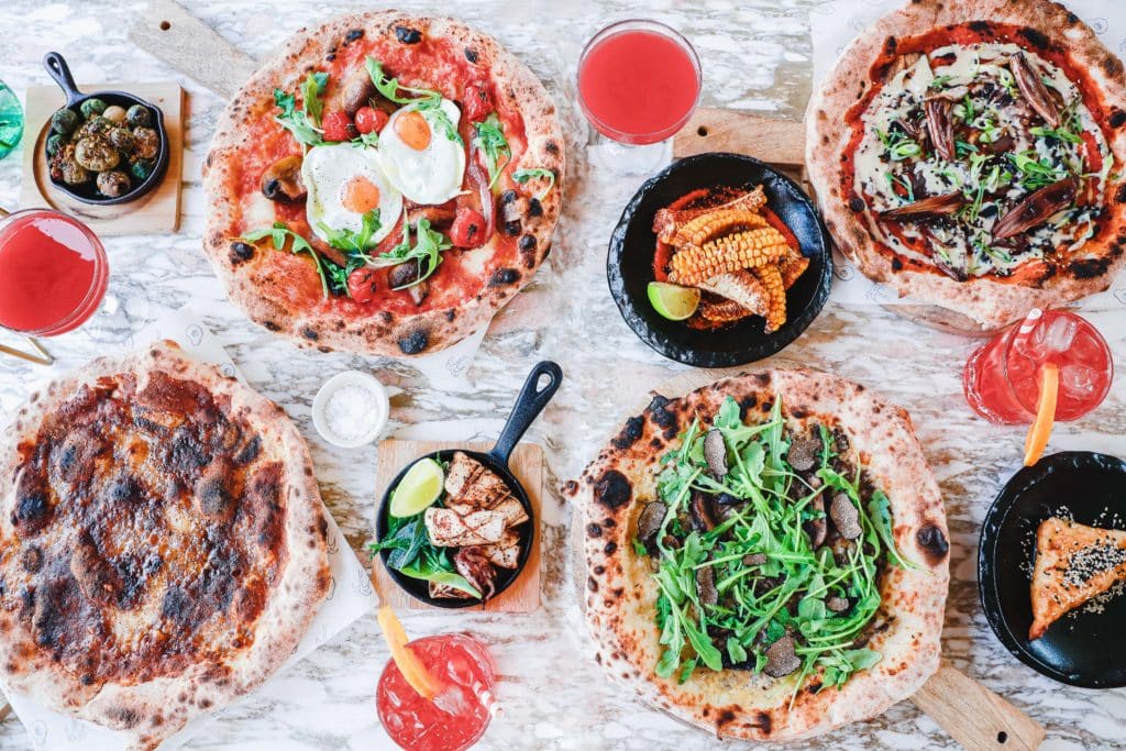 a selection of pizzas and side dishes laid out on a marble table, with toppings including fried eggs, and vegemite, from one of London's newest pizza places: Peggy Jean