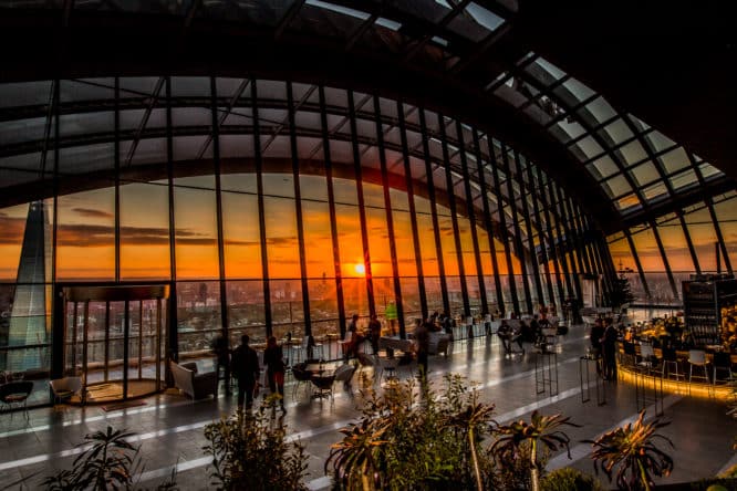 people sitting and standing around in front of the impressive skyline views from the sky garden as the sun sets