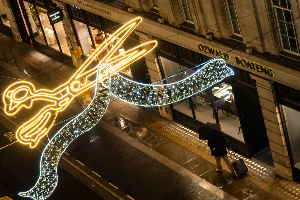 someone stood underneath a christmas lights display of golden shears above savile row