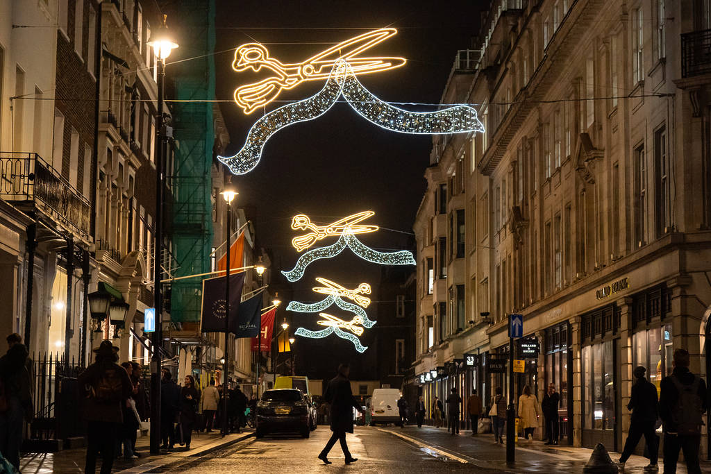 people walking beneath a christmas lights display of golden shears above savile row