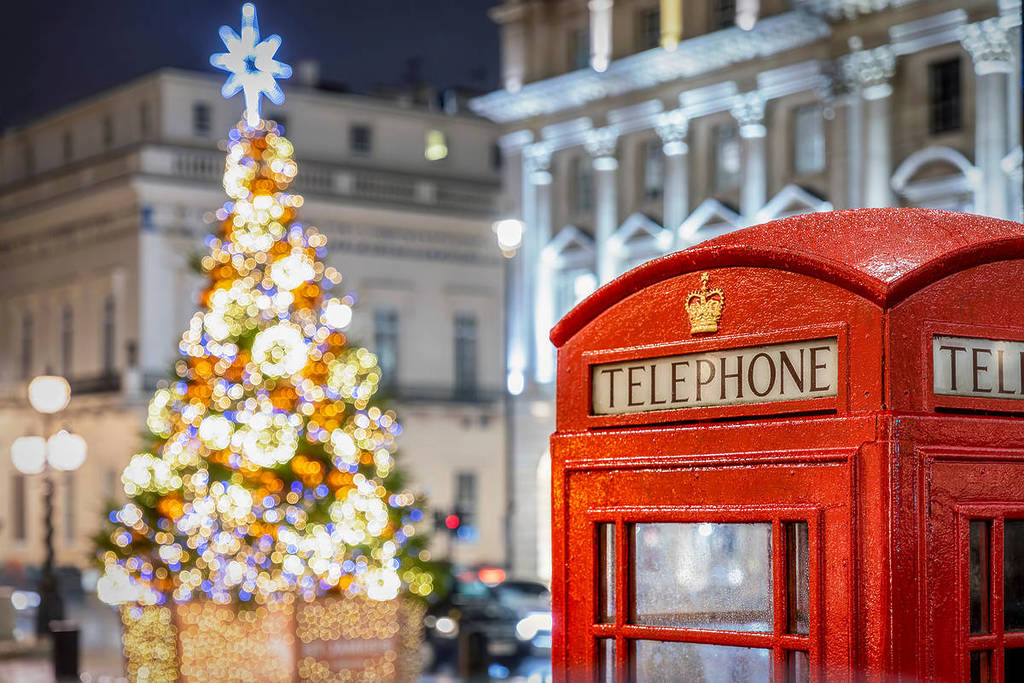 an iconic red telephone booth in front of an illuminated Christmas Tree in Central London at night