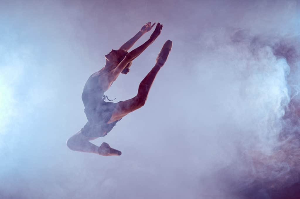 A ballet dancer leaping into the air during a ballet performance surrounded by mist
