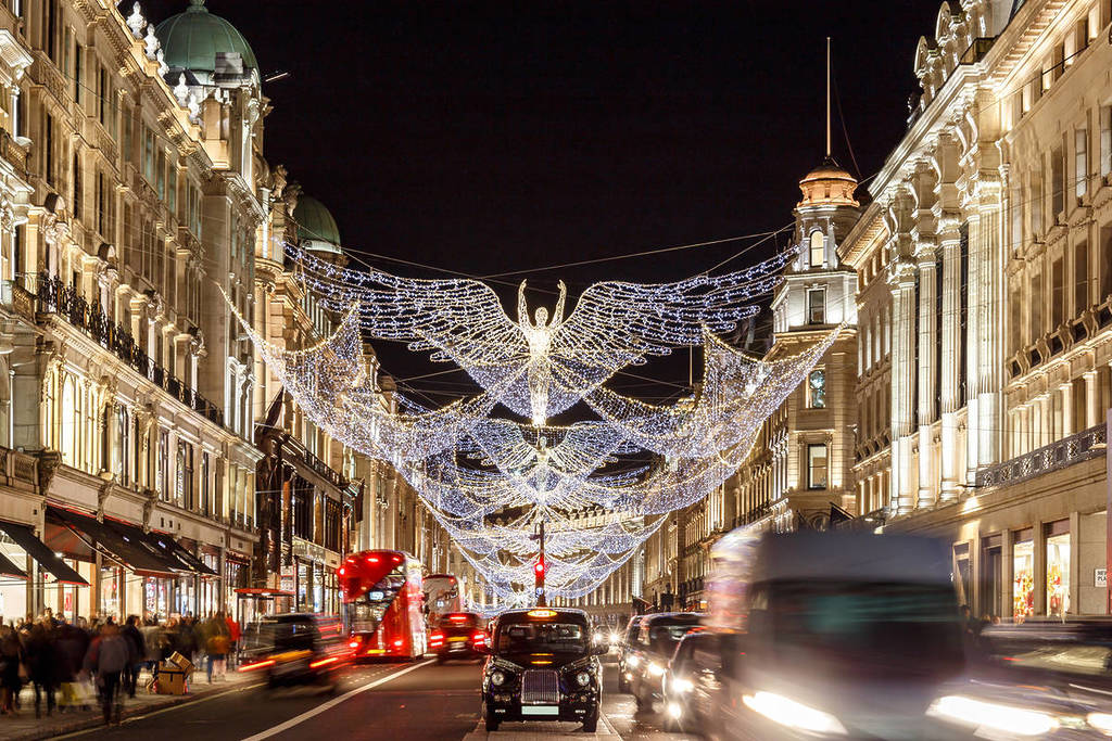 a nighttime shot of the 'spirit of christmas' christmas lights suspended over regent street, with cars, busses, and taxis whizzing by underneath