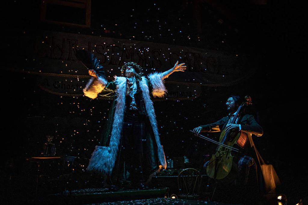 an actor onstage in the great christmas feast with a lantern in hand and snow falling on them