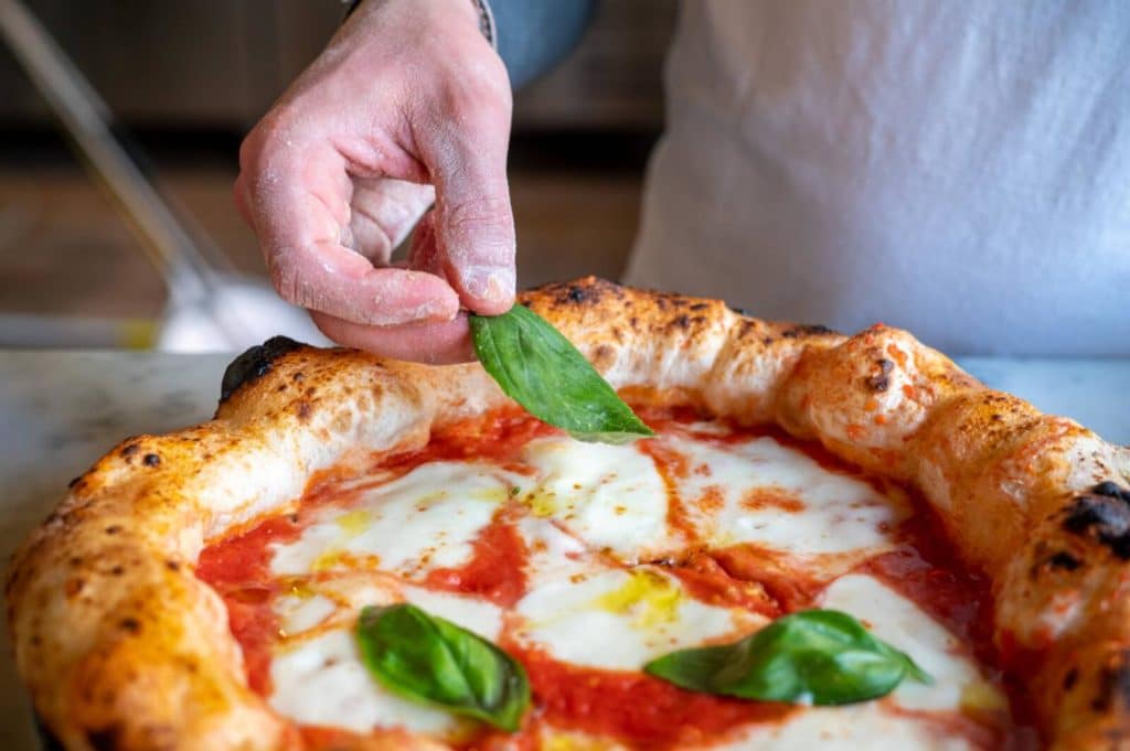 Someone lays a fresh basil leaf atop a margherita pizza from one of London's newest pizzerias, Vasiniko