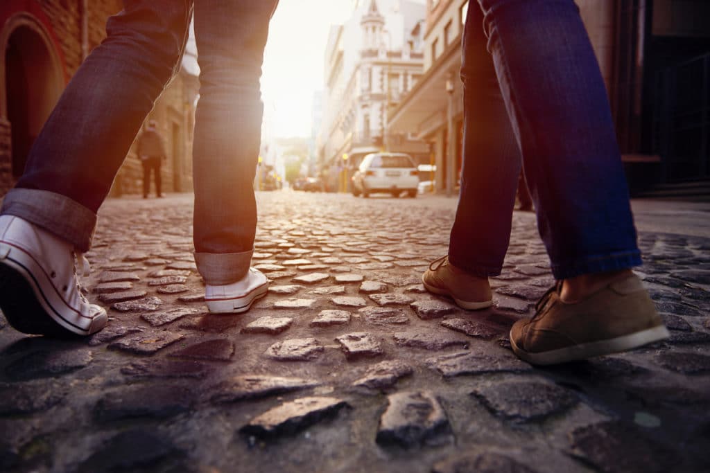 two people walking on cobblestones, only their legs from the knees down and the cobbled floor are visible