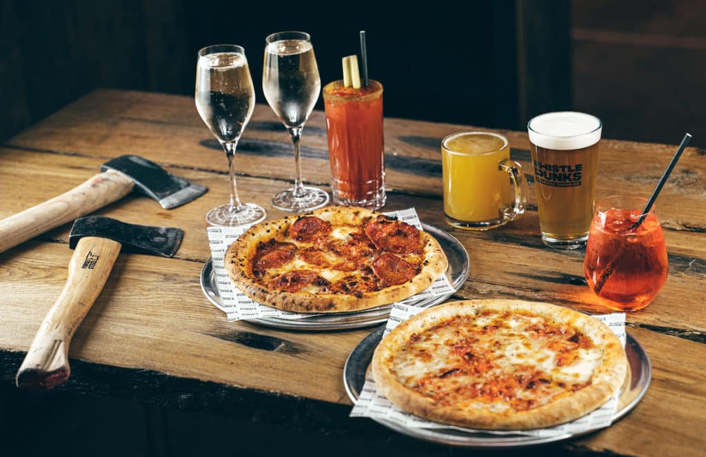 a selection of drinks and pizzas arranged on a table next to some throwing axes