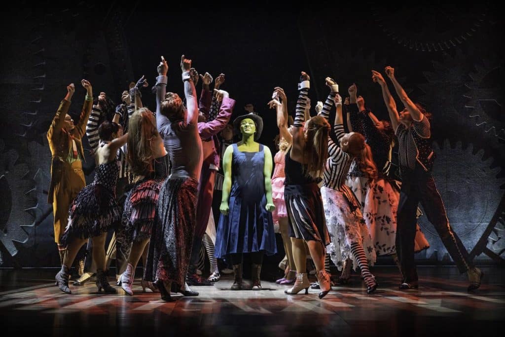 A women with green skin (Elphaba)- on stage surrounded by people with arms raised
